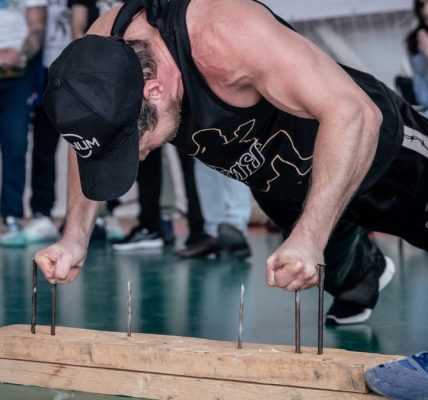 A man doing finger push-ups on nails during a gym competition with spectators watching.
