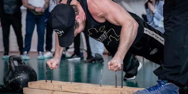 A man doing finger push-ups on nails during a gym competition with spectators watching.