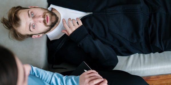 A man lying on a couch during a therapy session with a counselor in a modern office setting.
