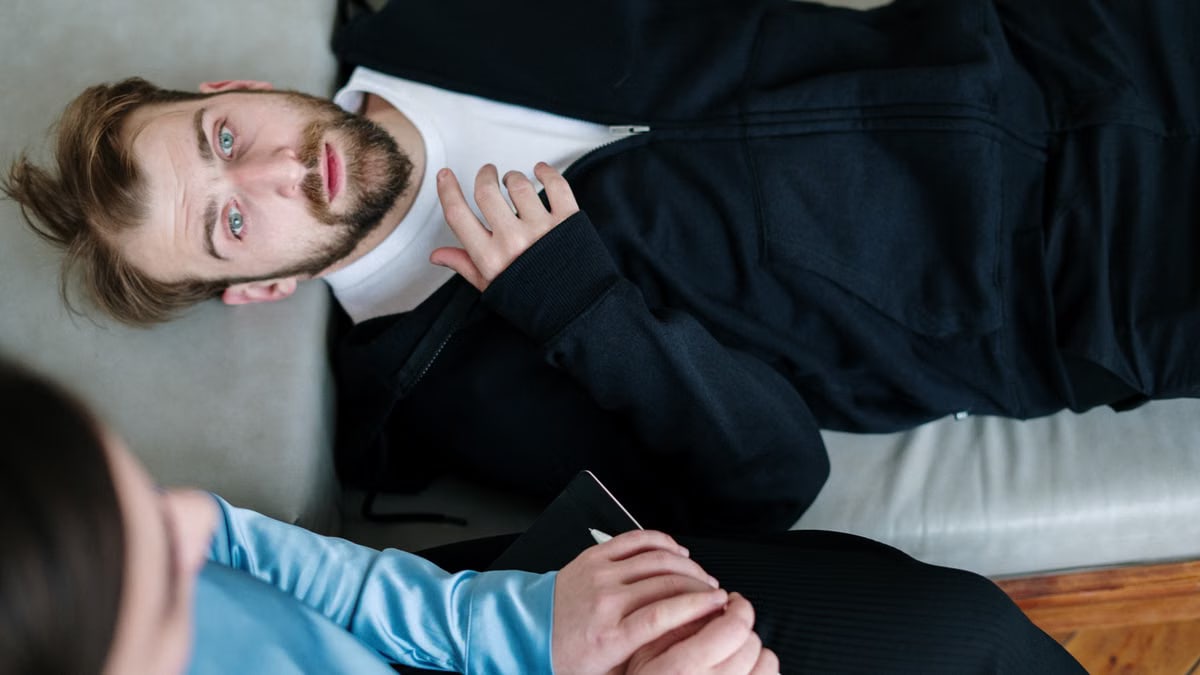 A man lying on a couch during a therapy session with a counselor in a modern office setting.